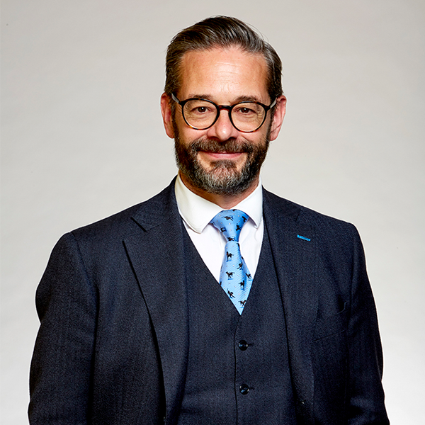 A man with a beard wearing a suit, glasses, and smiling 