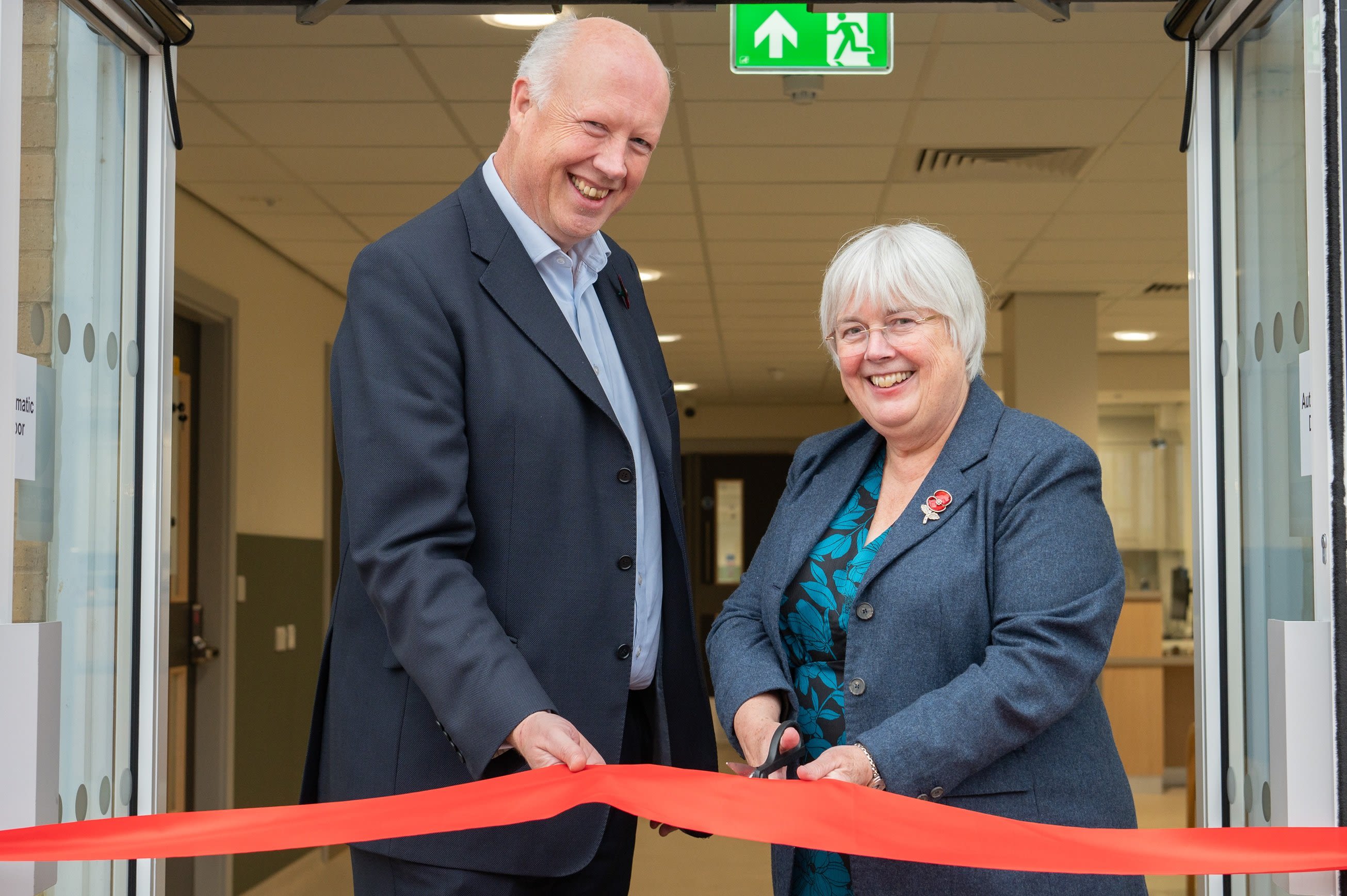 A man and woman, dressed in suits, cutting a red ribbon to open a new building